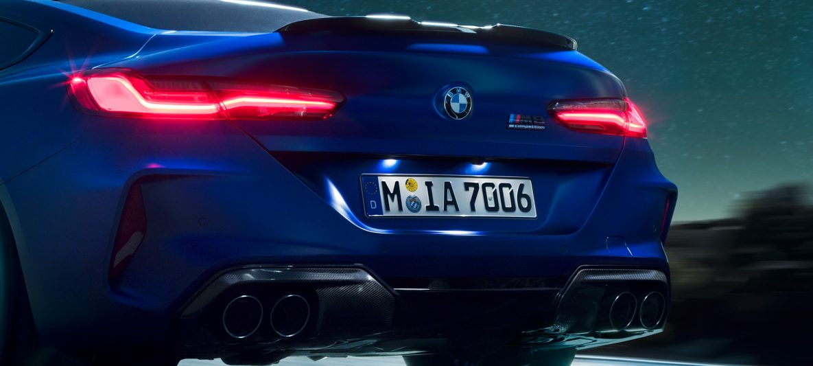 BMW M8 Competition Coupé in Marina Bay Blau metallic, Nahaufnahme Heck bei Nacht mit M Diffusor in Carbon Schwarz.